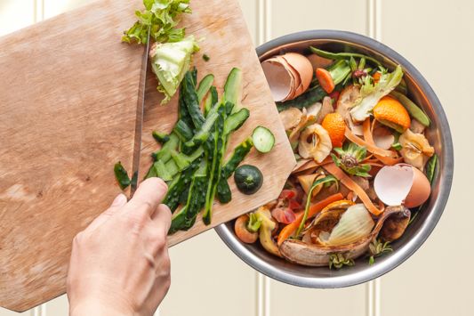 Hand schiebt Lebensmittelreste in den Bio Müll