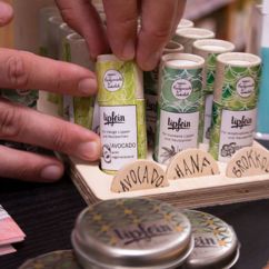 Zwei Hände greifen nach einem Lippenpflegestift der Marke Lipfein, daneben weitere Naturkosmetik