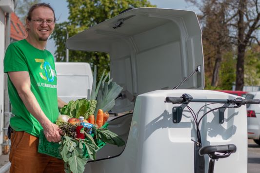 Mann hebt Kiste voller Lebensmittel auf Lastenrad