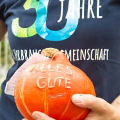 Eine Hand hält einen Kürbis mit der Aufschrift "Alles Gute", dahinter ein Jubiläums-Shirt der VG mit der Aufschrift "30 Jahre VG Verbrauchergemeinschaft"