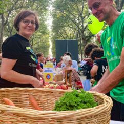 Im Vordergrund ein Korb mit Bio-Gemüse und Käuter, dahinter Mitarbeiter der VG Verbrauchergemeinschaft eG an einem Tisch