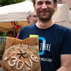 Vorstandmitglied der VG Verbrauchergemeinschaft eG zeigt Jubiläumsbrot mit der Aufschrift "30 Jahre VG"