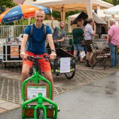 Ein Mann auf einem Lastenrad, im Hintergrund ein Stand des ADFC