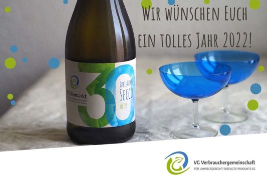 Eine Flasche VG Jubiläums-Secco mit Gläsern auf einem Tisch, im Bild der Text "Wir wünschen Euch ein tolles Jahr 2022!"