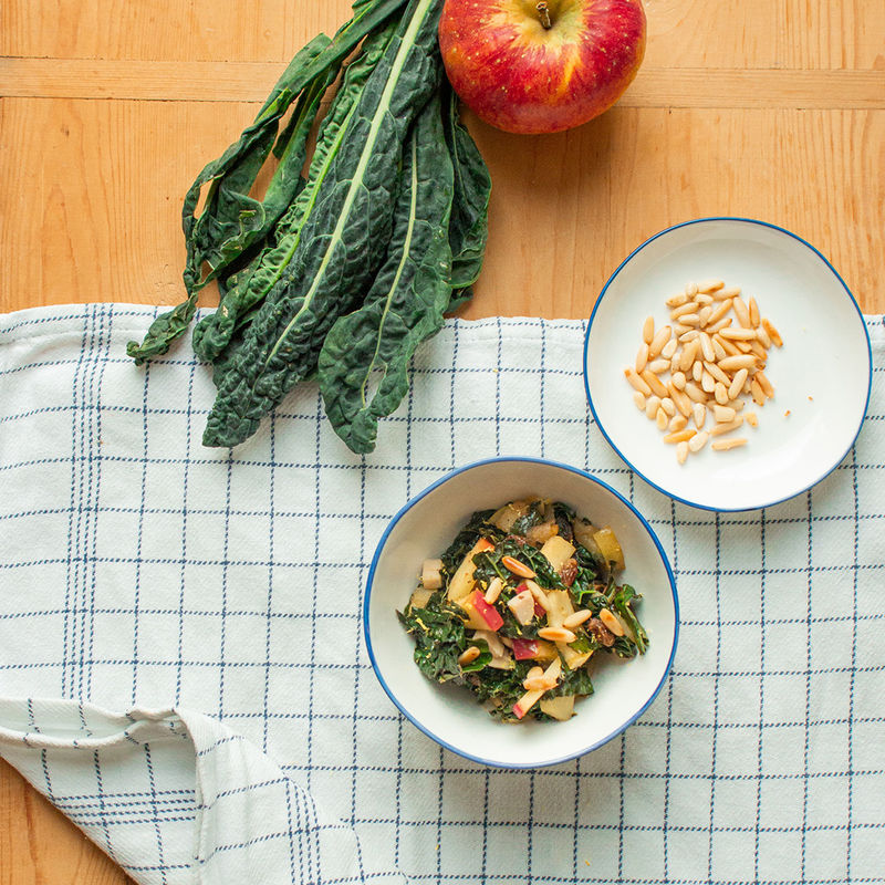 Salat aus Apfel und Grünkohl in einer Schüssel, daneben die einzelnen Zutaten auf einem Brett