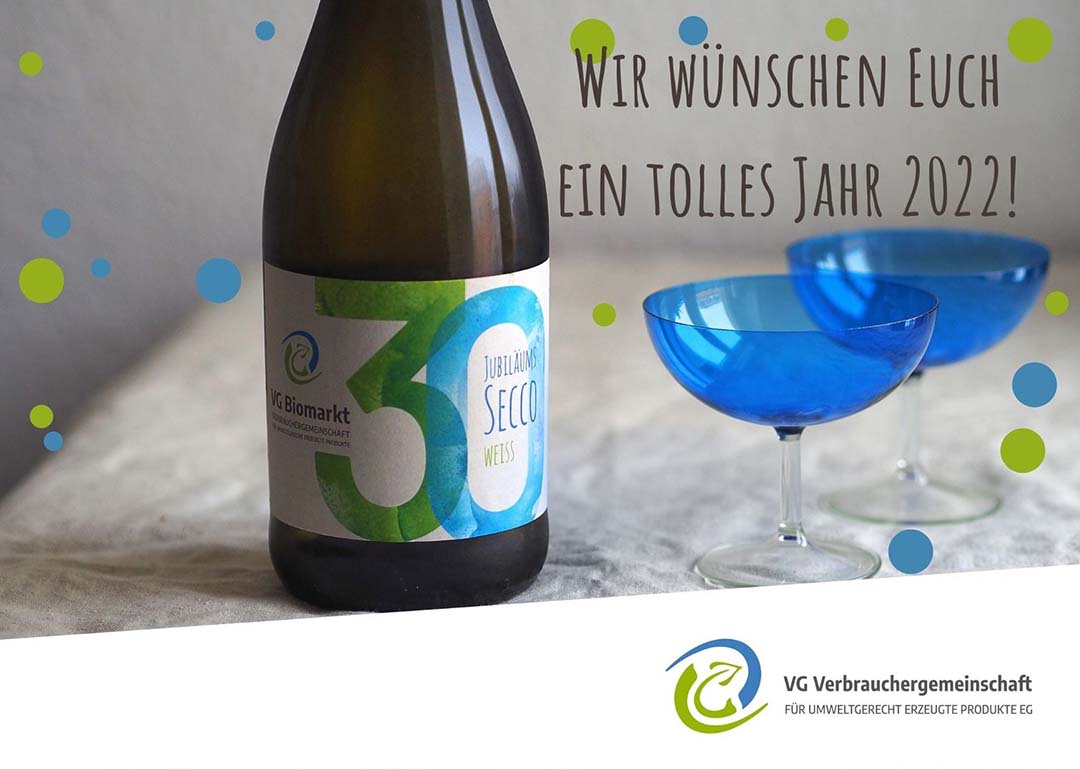 Eine Flasche VG Jubiläums-Secco mit Gläsern auf einem Tisch, im Bild der Text "Wir wünschen Euch ein tolles Jahr 2022!"